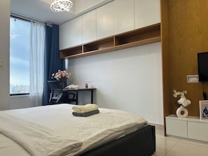 A modern hotel room with a large bed, a desk with a chair, a television, and a view of the city through the window. - RiverGate Suite – Upscale Apartment Near Ben Thanh Market (Thành phố Hồ Chí Minh)