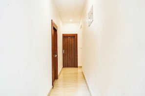 A narrow hallway with a wooden door at the end, white walls, and a light fixture on the ceiling. - Hotel O Golden Pearl (Bhopal)