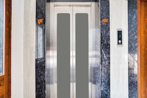 An elevator with a metallic interior, a control panel with a green indicator, and two vertical panels with orange text. - Hotel O Golden Pearl (Bhopal)