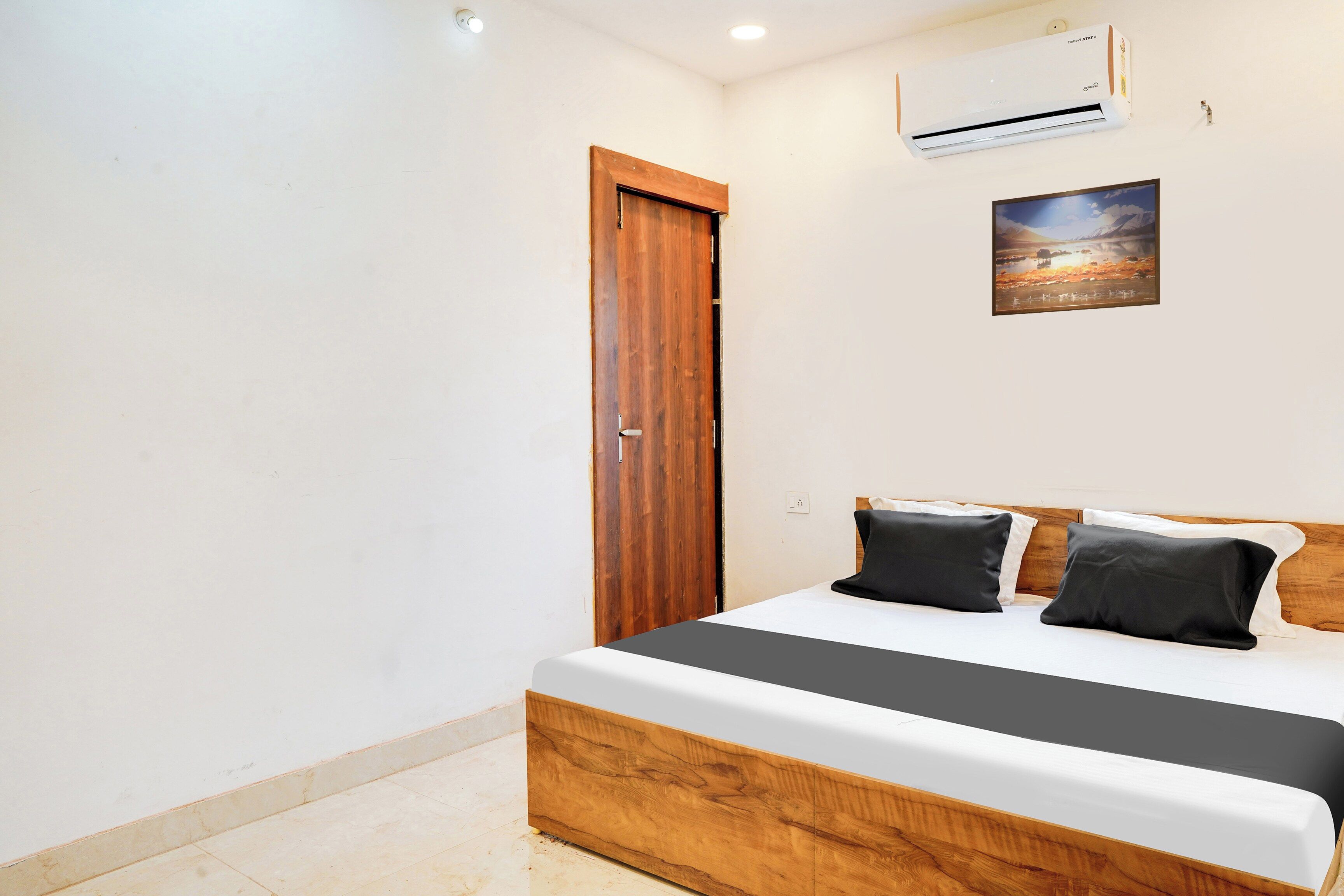 Een slaapkamer met een houten bedframe, een witte matras en twee zwarte kussens.