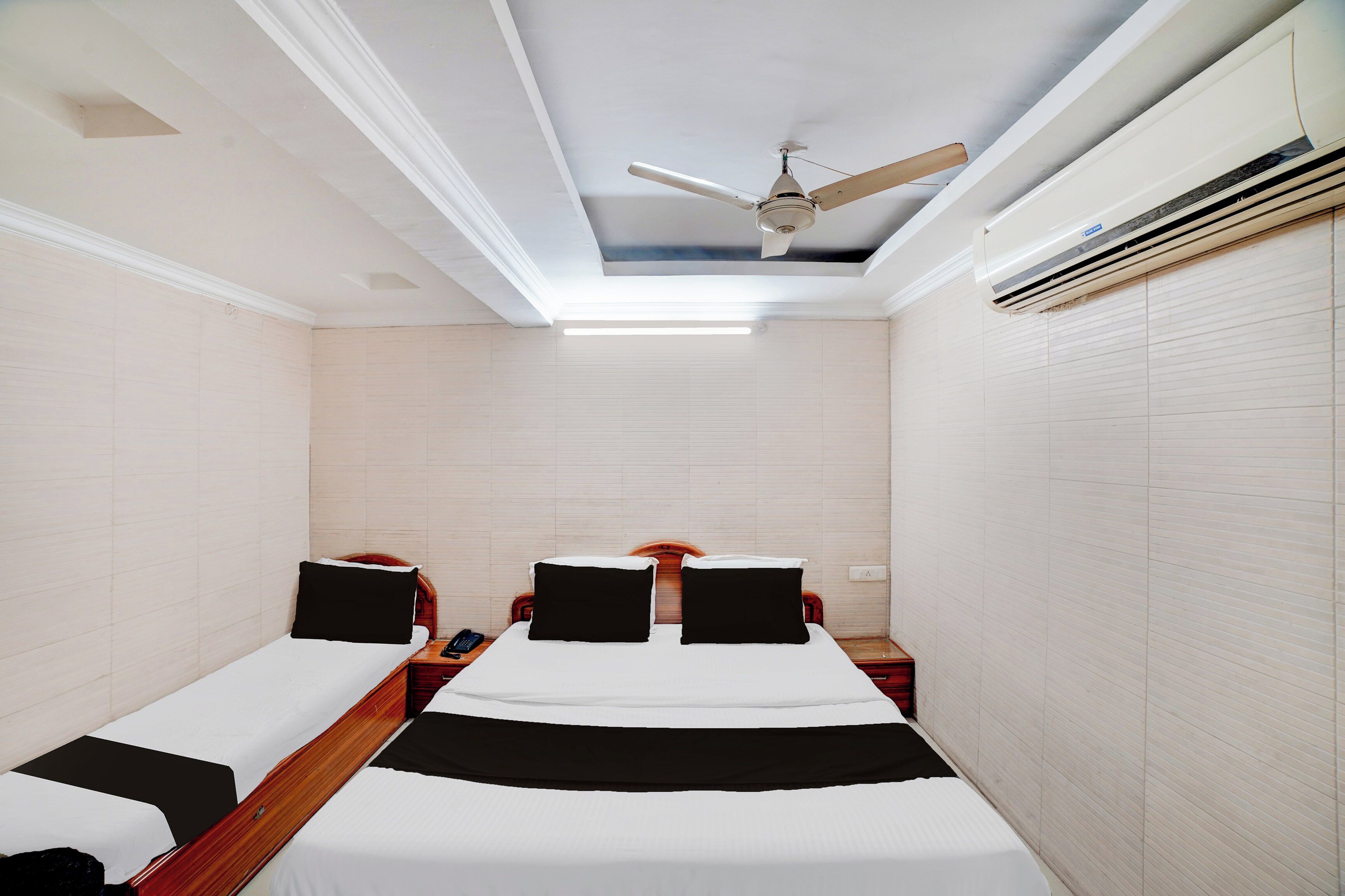Habitación de hotel con dos camas, ventilador de techo y unidad de aire acondicionado.