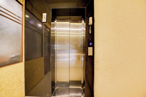 Ein Aufzug mit metallischem Innenraum, einem Bedienfeld mit digitaler Anzeige und einem an der Wand montierten Telefon.