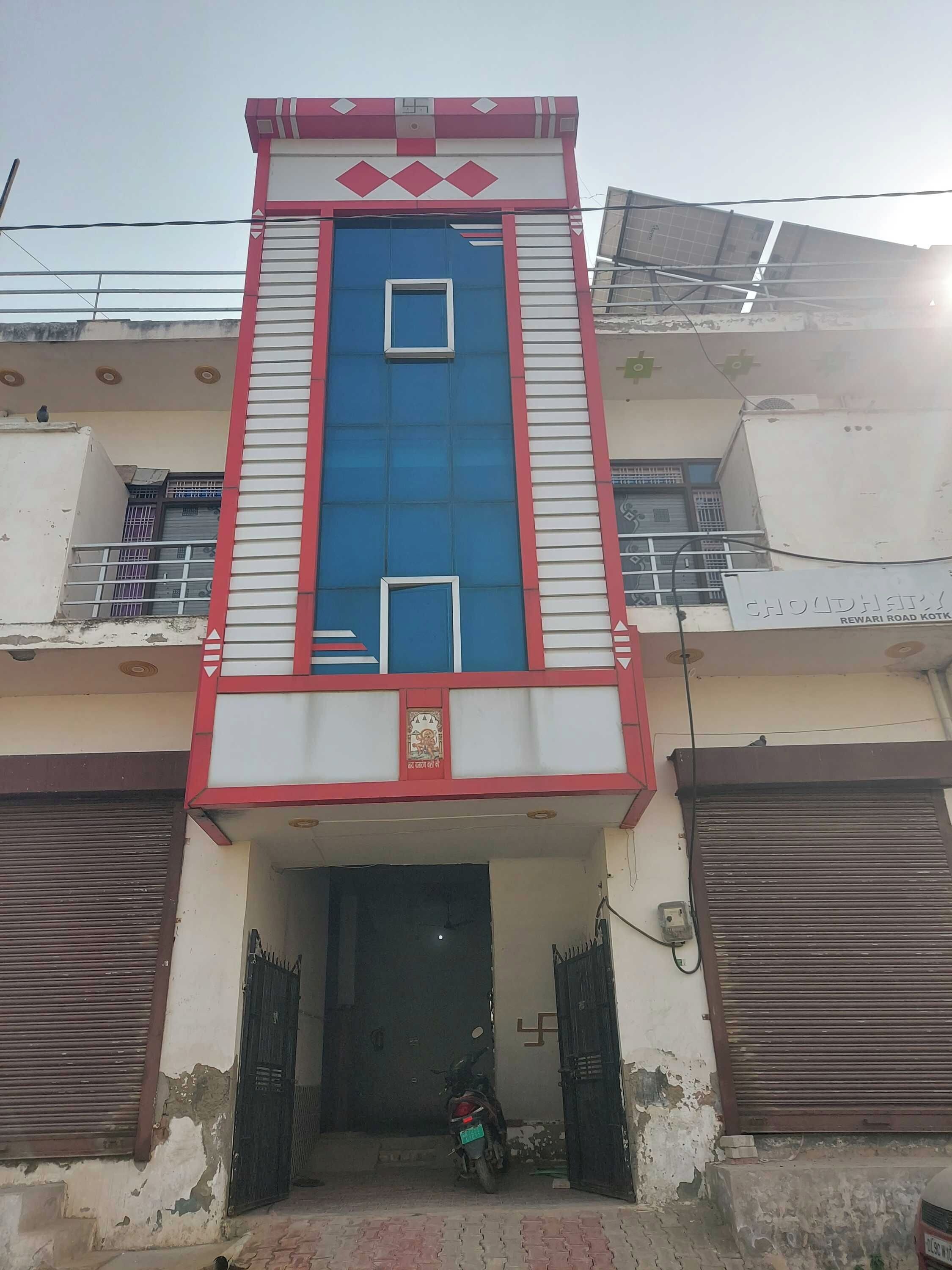 A building with a central blue and red facade, a gated entrance, and a visible motorcycle.