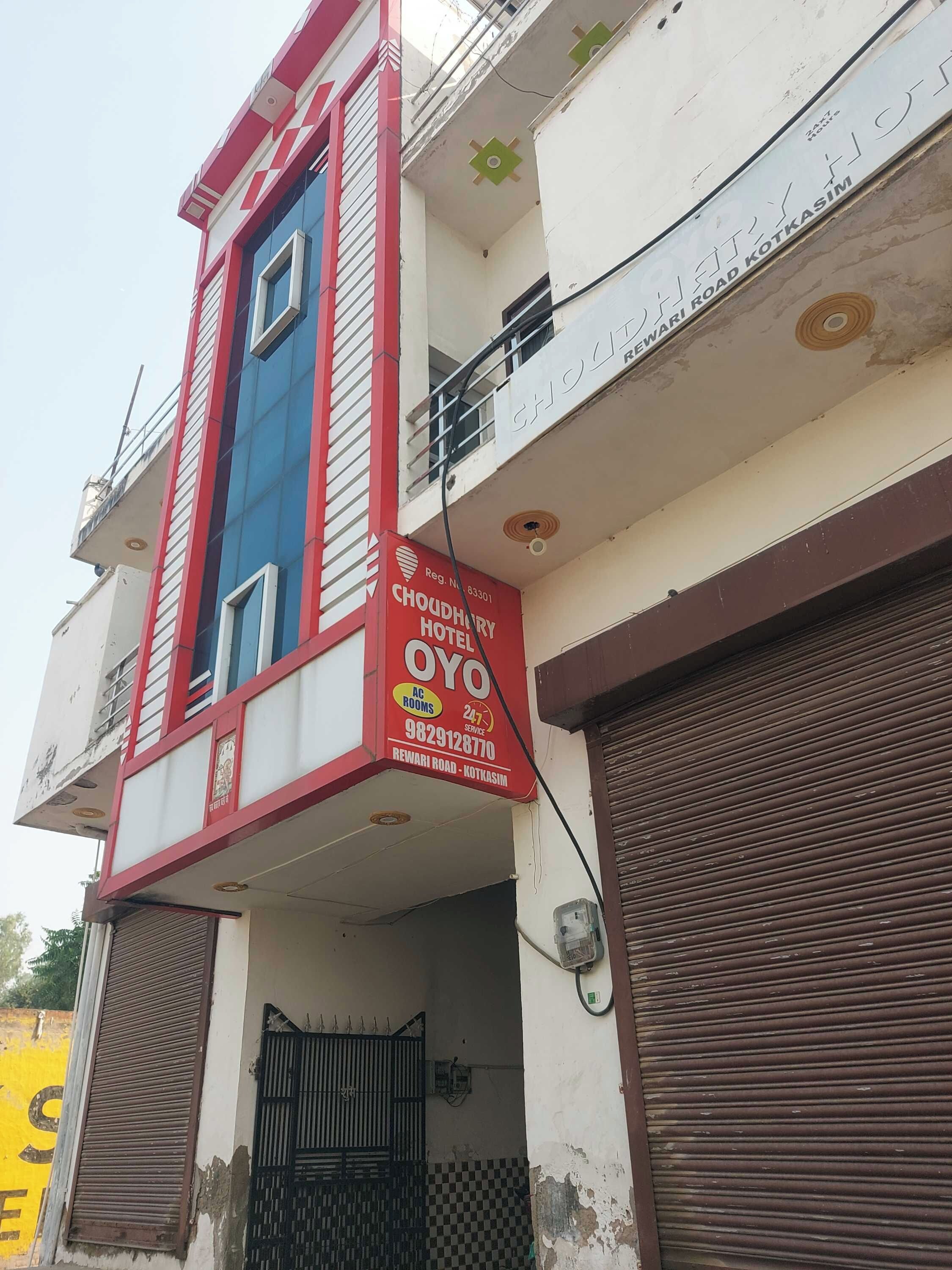 A hotel with a red and white facade, a balcony, and a sign indicating it is on Rewari Road.