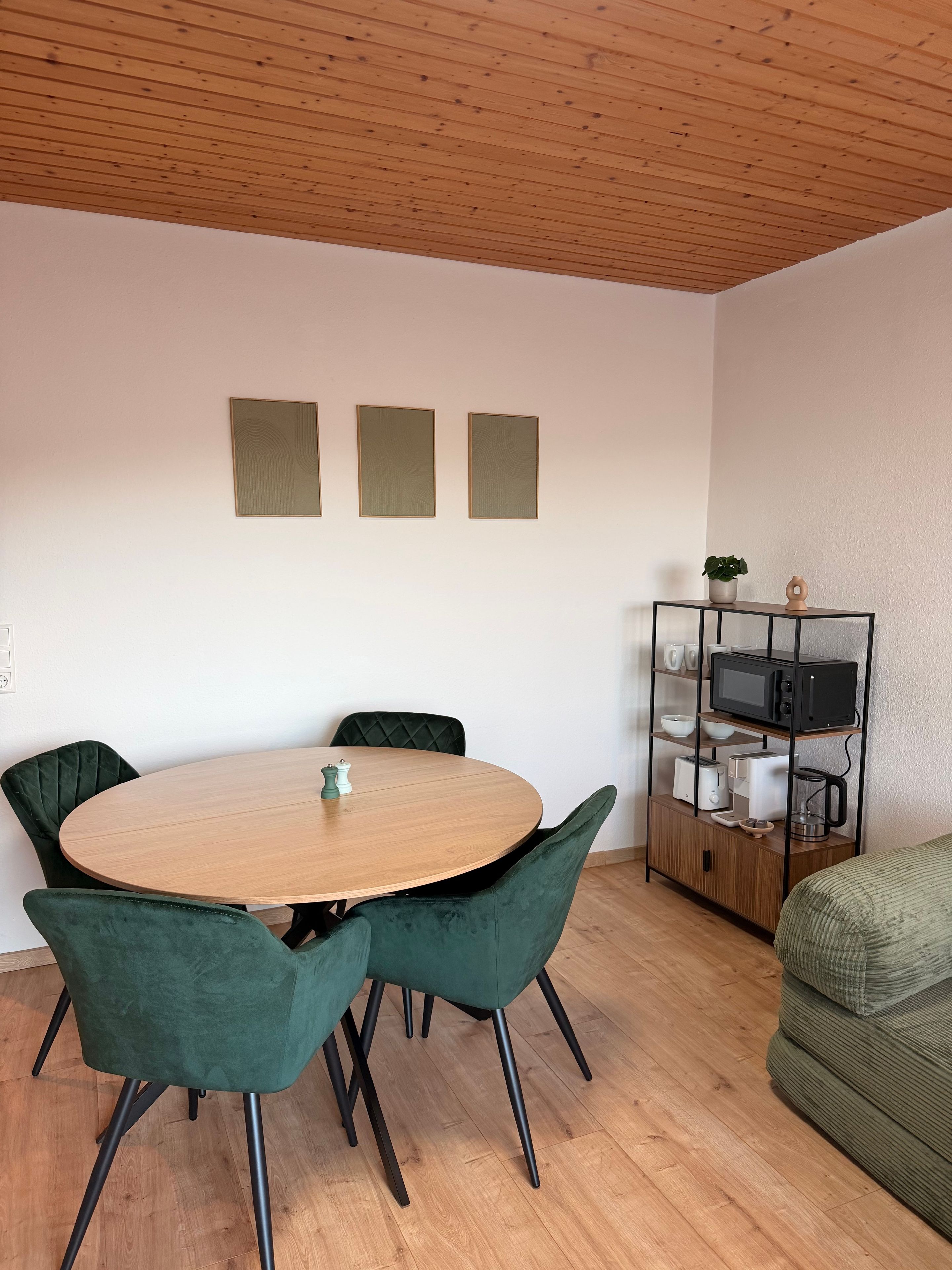 A dining area with a round table, four chairs, a cabinet with kitchen appliances, and a green sofa.