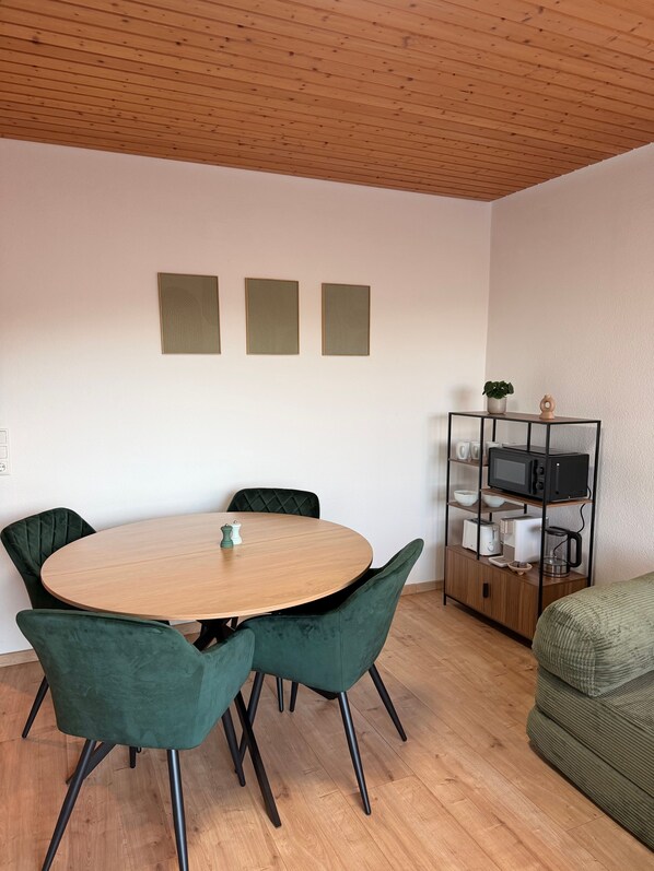 A dining area with a round table, four chairs, a cabinet with kitchen appliances, and a green sofa. - Modern 2-Room Holiday Apartments Triberg (Triberg im Schwarzwald)