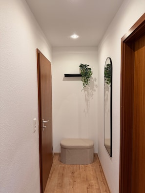 A narrow hallway with wooden flooring, a bench, a wall-mounted shelf with a plant, and a mirror. - Modern 2-Room Holiday Apartments Triberg (Triberg im Schwarzwald)