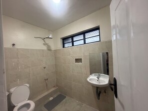 Une petite salle de bain carrelée, équipée de toilettes, d’une douche et d’un lavabo.