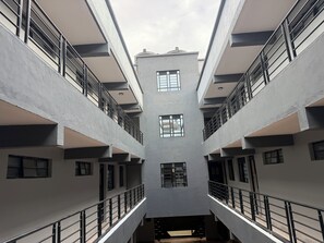 Un immeuble à plusieurs étages doté d’un atrium central, de balcons et d’une série de fenêtres.