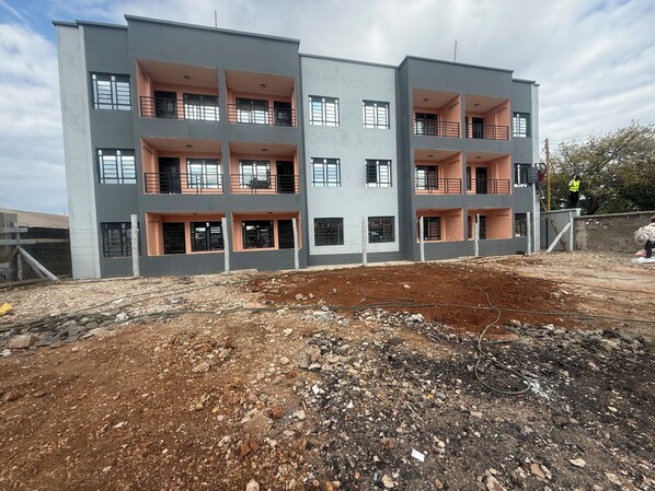 Un immeuble à plusieurs étages doté de balcons, un chantier de construction en face et un ouvrier sur le toit.
