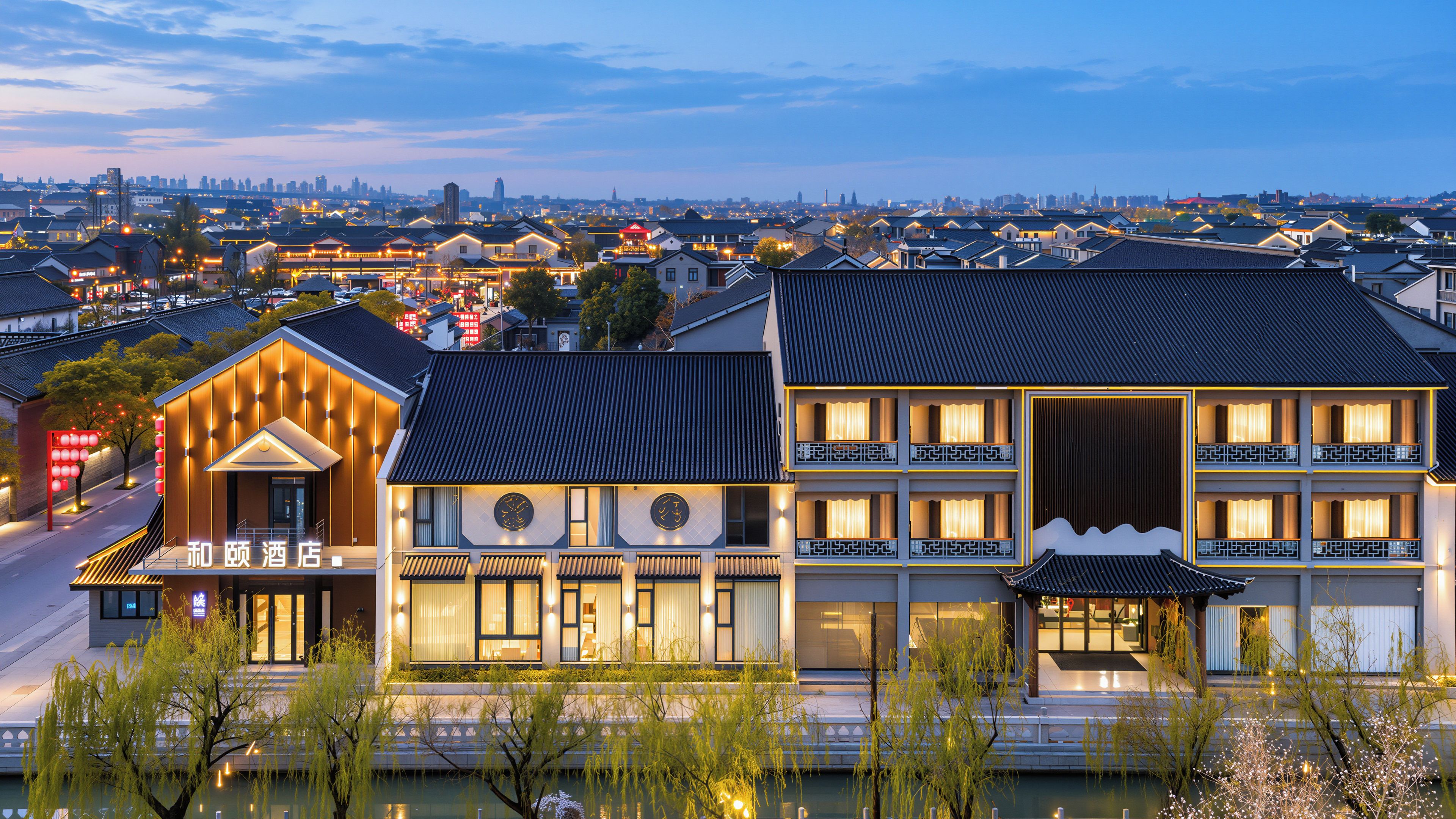 Een hotel met traditionele architectuur, een modern gebouw ernaast en een uitzicht op een stadsbeeld op de achtergrond.