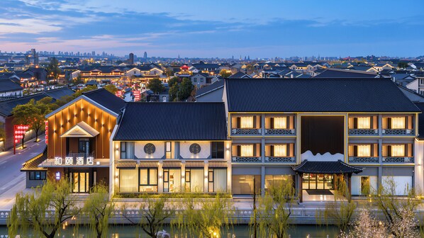 Un hôtel à l’architecture traditionnelle, un bâtiment moderne attenant, et une vue sur le paysage urbain en arrière-plan.