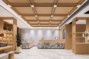 Un espace d’accueil moderne, avec un comptoir de réception en bois, un sol en marbre et une grande plante en pot.