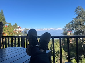 A person seated on a wooden deck with a view of a mountain range and buildings in the background. - Charming 3-bedroom house in Suryabinayak perfect for your stay (Suryabinayak)