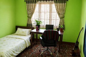 A room with a bed, a desk with a laptop, a chair, a guitar, and two potted plants. - Charming 3-bedroom house in Suryabinayak perfect for your stay (Suryabinayak)