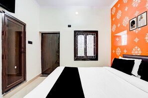 A hotel room with a bed, a window with bars, an orange patterned wall, and a door. - Hotel O Mahadev Palace (Patna)