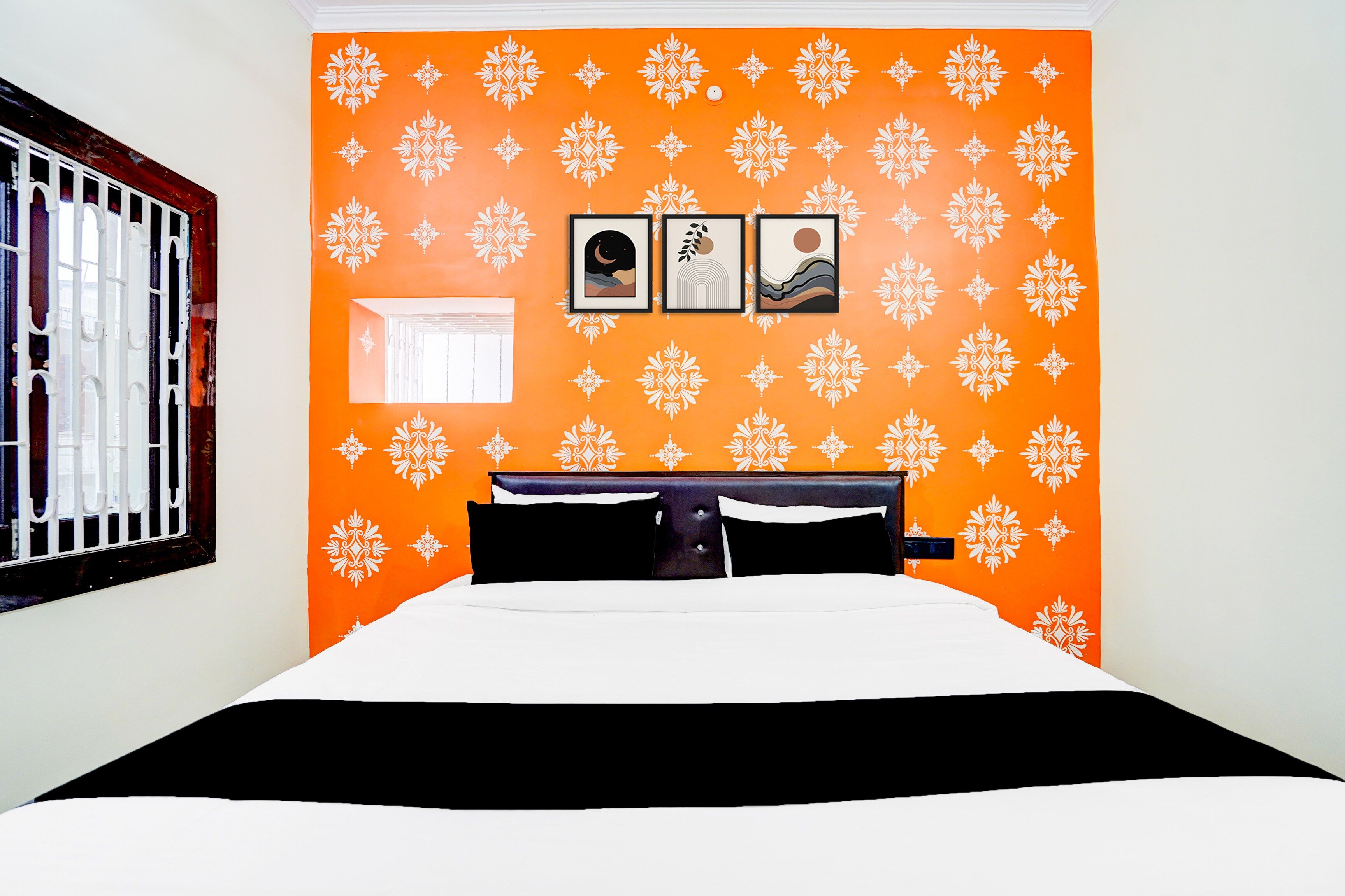 Ein Zimmer mit einer orangefarbenen Wandmusterung, einem Bett mit schwarz-weißer Bettwäsche und drei gerahmten Bildern.