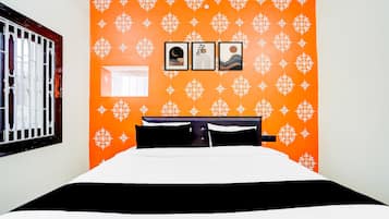 Ein Zimmer mit einer orangefarbenen Wandmusterung, einem Bett mit schwarz-weißer Bettwäsche und drei gerahmten Bildern.