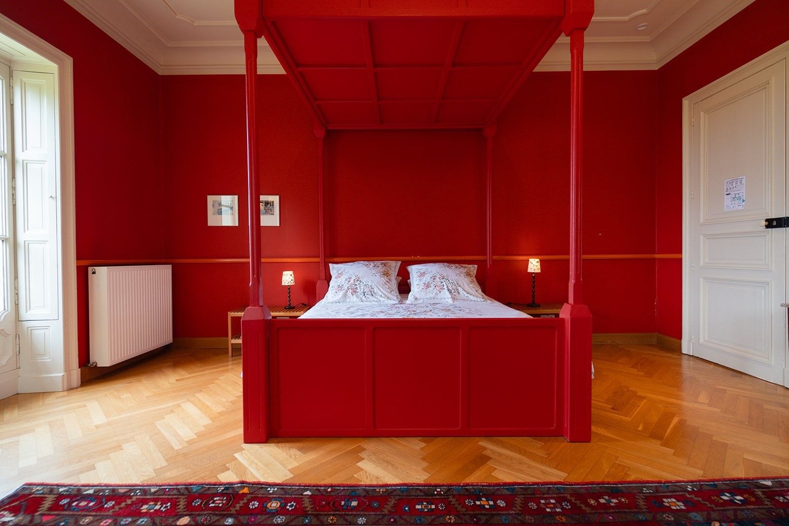 Ein rotes Himmelbett in einem Zimmer mit Holzboden und einem gemusterten Teppich.