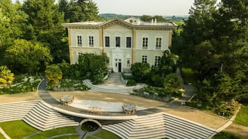 A large, two-story building with a symmetrical facade, a central entrance, and a landscaped garden with a circular patio and seating area.