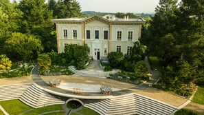 Un grand bâtiment à deux étages, doté d’une façade symétrique, d’une entrée centrale et d’un jardin aménagé avec un patio circulaire et un espace détente.