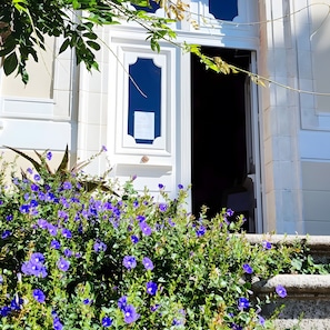 Un edifici amb façana blanca, una porta amb marc blau i una finestra amb un avís encarregolit.