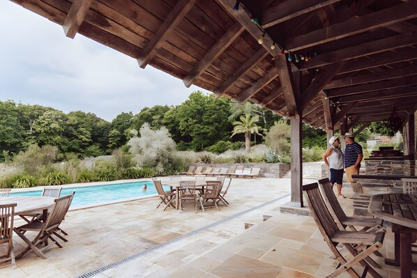 Un espace piscine extérieur avec des meubles en bois et un coin salon abrité.