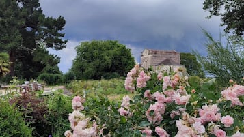 A garden with a stone building, lush greenery, and pink flowers.