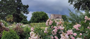 Un jardin agrémenté d’un bâtiment en pierre, d’une végétation luxuriante et de fleurs roses.