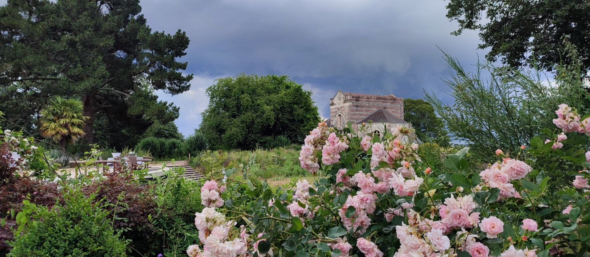 A garden with a stone building, lush greenery, and pink flowers.