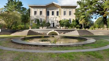 Un grand bâtiment de style classique, doté d’une façade symétrique, d’une entrée centrale avec des marches et d’une fontaine circulaire en premier plan.