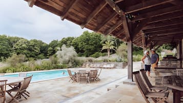 An outdoor pool area with wooden furniture and a covered seating area.