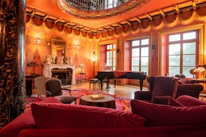 Una sala espaiosa amb una llar de foc, un piano i mobles tapissats de vermell.