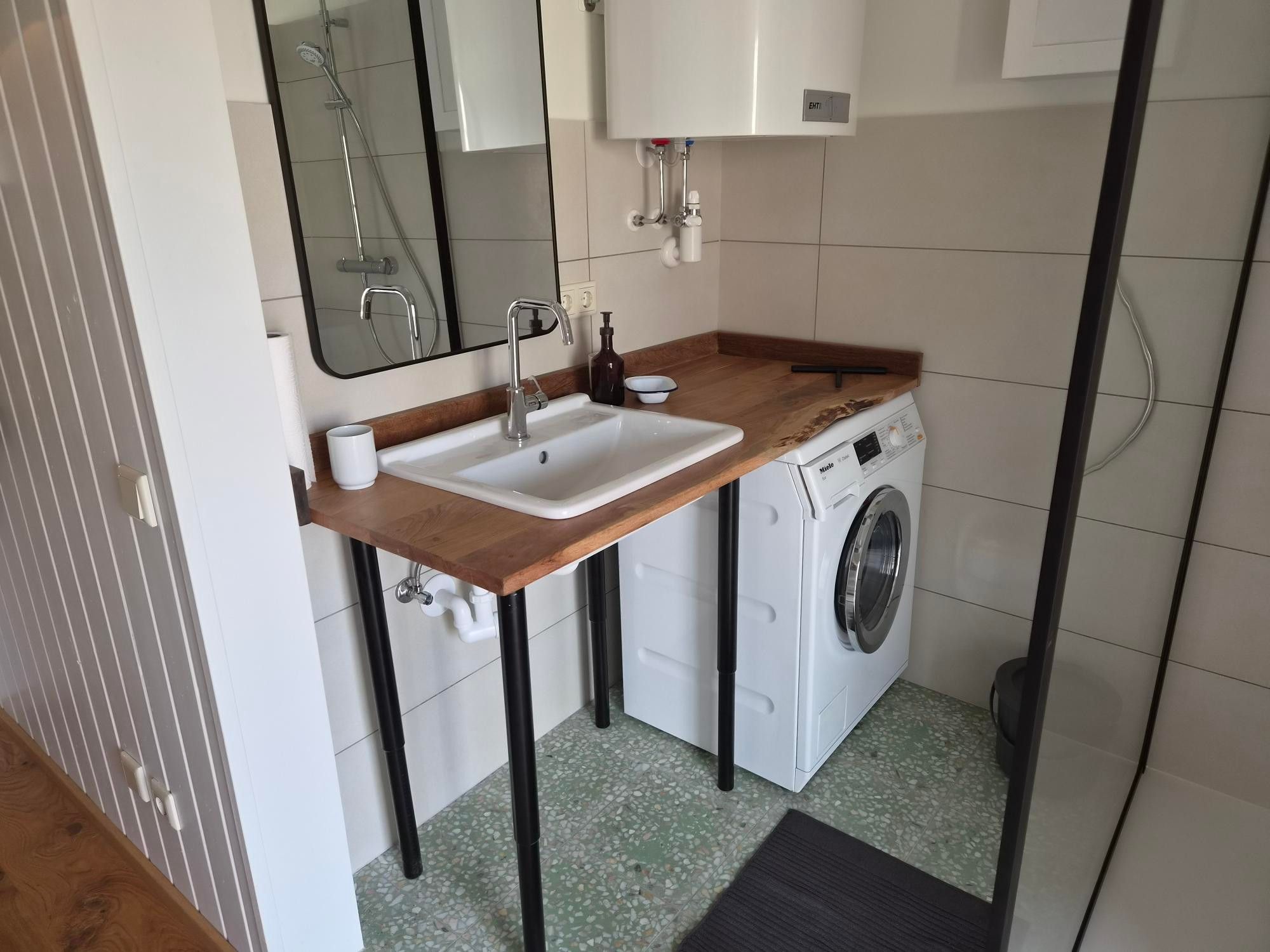 A compact bathroom with a wooden countertop sink, a washing machine, and a mirror.