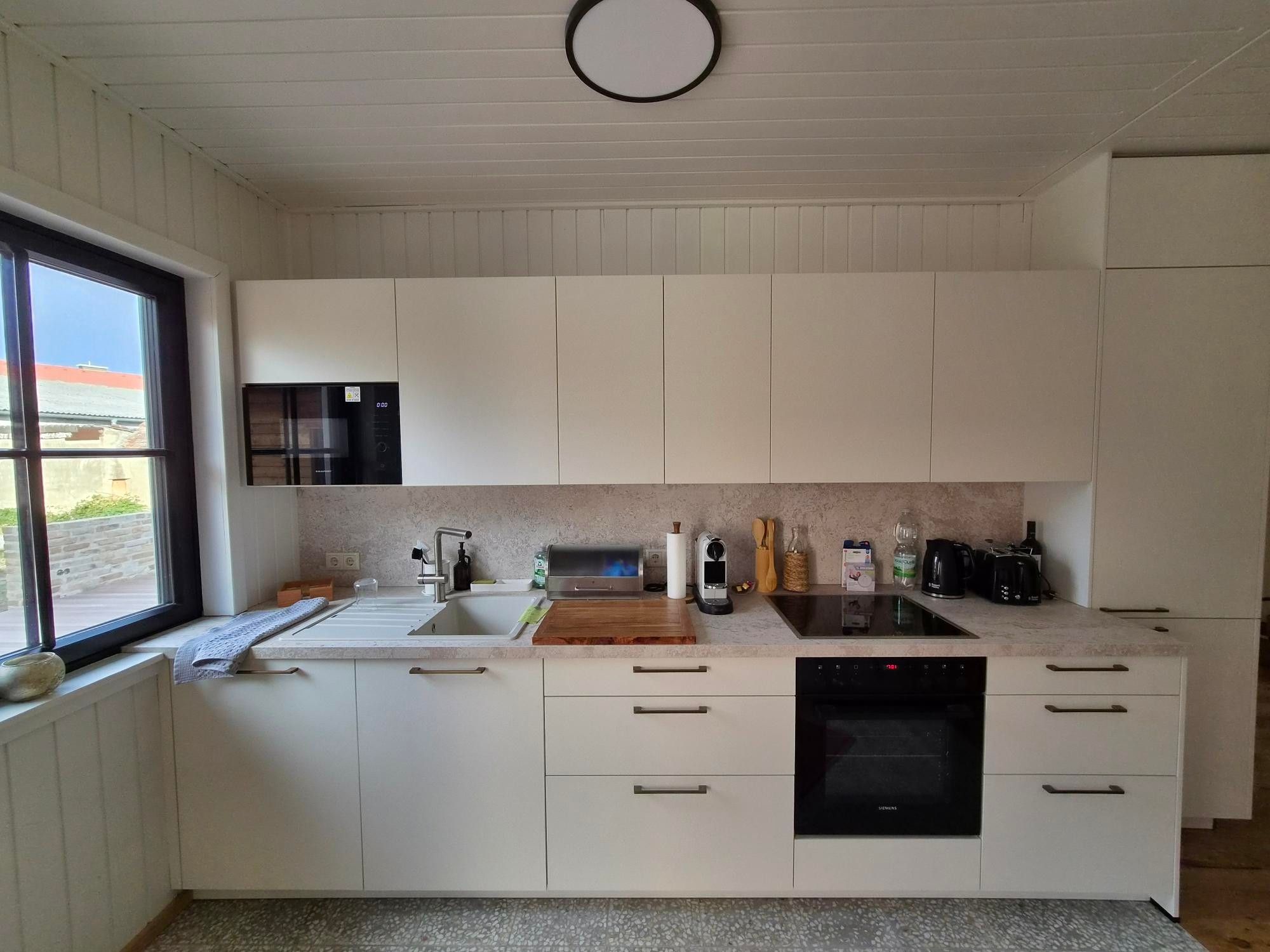 Eine moderne Küche mit weißen Schränken, einem eingebauten Ofen und einem Fenster mit Blick nach draußen.
