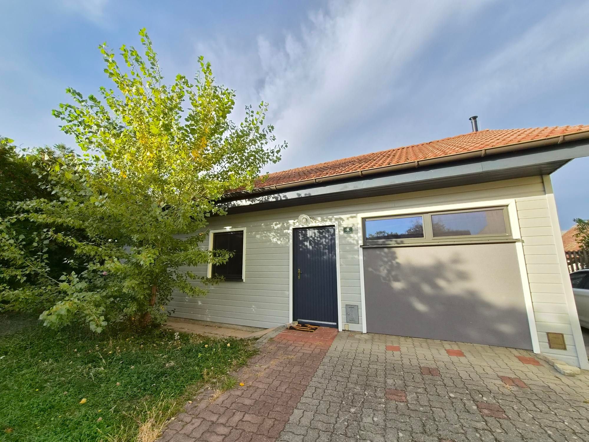 Einbungalow mit Garage, kleiner Veranda und einem Baum im Garten.