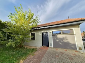 Einbungalow mit Garage, kleiner Veranda und einem Baum im Garten.