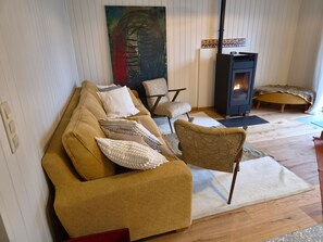 Ein Wohnzimmer mit einer Couch, Sesseln, einem Teppich, einem Gemälde und einem Kaminofen.