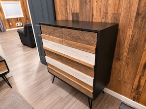 A wooden dresser with drawers and a black top, placed in a room with wooden flooring and a dark wall.
