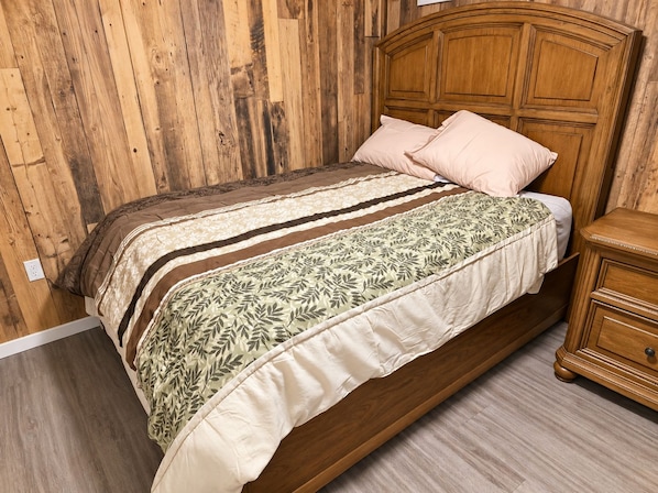 A wooden bed with a headboard, a bedside table, and a patterned bedspread.