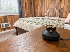 A room with a wooden bed, a glass lamp on a wooden table, and a window with blinds.