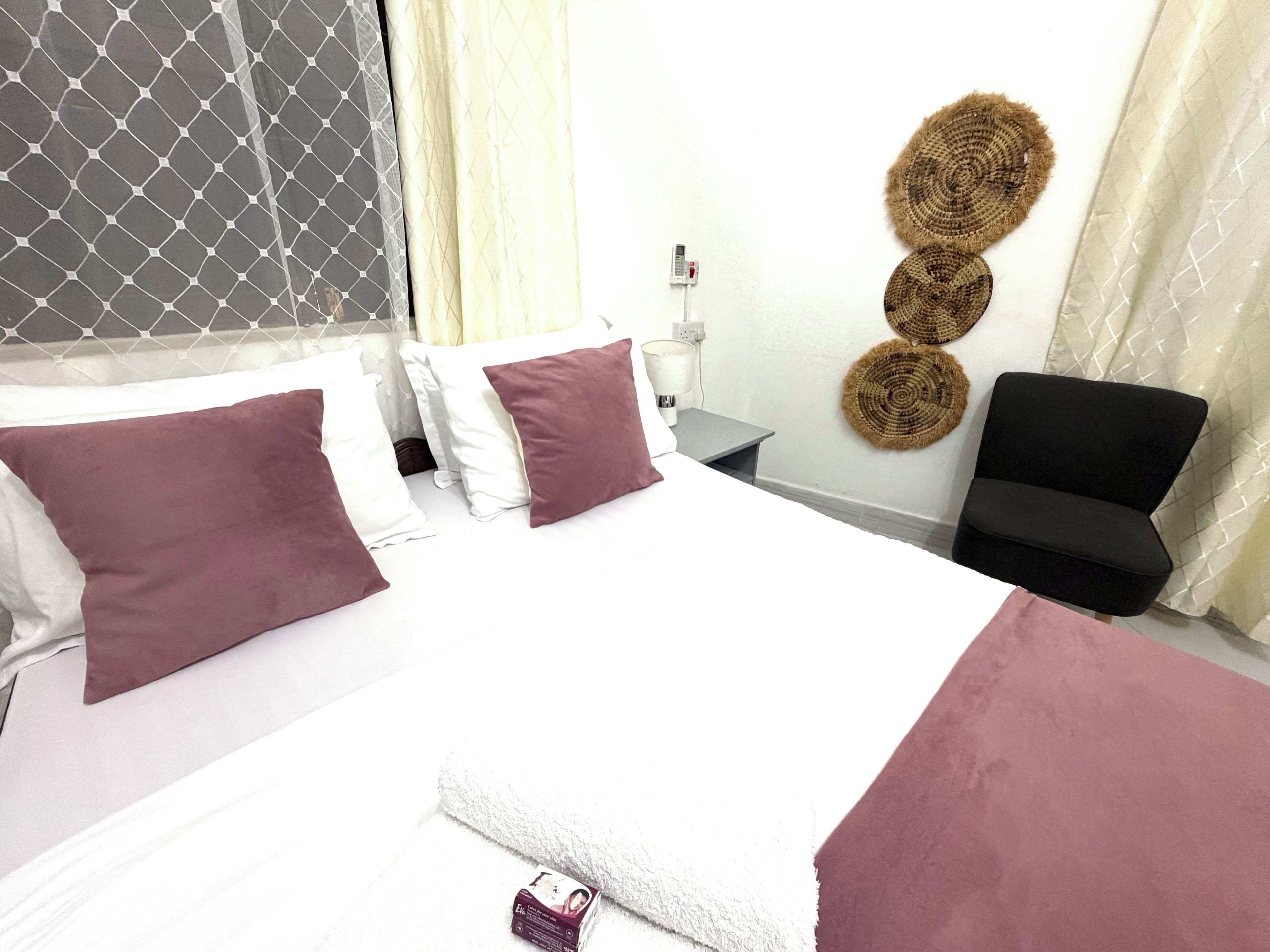Una habitación de hotel con cama, almohadas, mesita de noche, una silla y adornos en la pared.