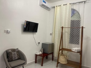 A room with a television mounted on the wall, a small table with a kettle, a chair, and a wooden rack with towels. - NASHU HOUSE STONE TOWN (Zanzibar)