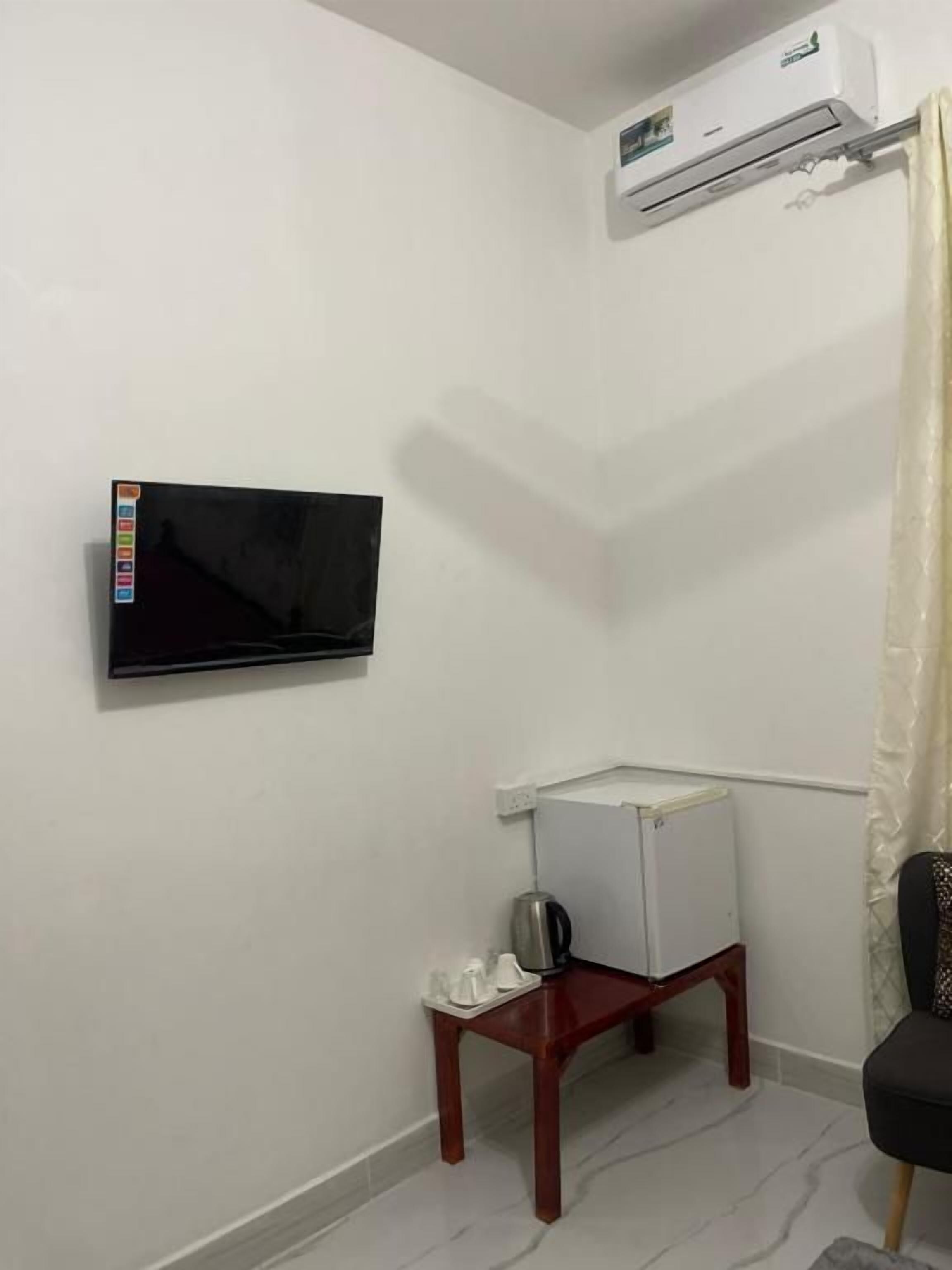 A room with a mounted television, a small table with a kettle, and a white radiator.