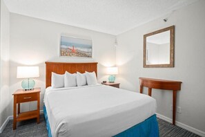 Quarto de hotel com uma cama grande, duas mesas de cabeceira com luminárias, um painel de cabeceira de madeira, um espelho fixado na parede e um quadro emoldurado acima da cama.