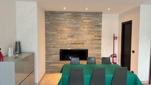 A modern dining area with a stone wall, a flat-screen TV, and a green tablecloth. - New Listing (Roma)