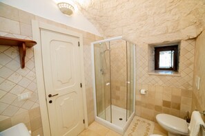 A bathroom with a shower enclosure, toilet, and a small window. - New Listing (Puglia)