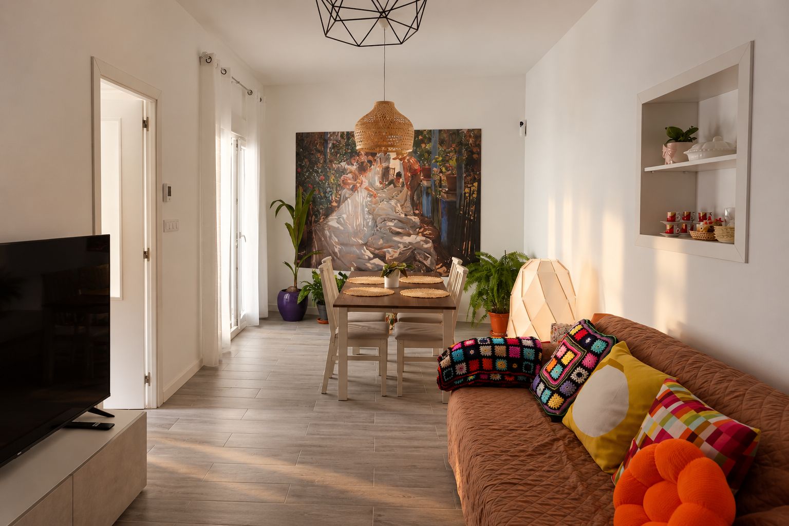 A modern living room with a television, a dining area with a table and chairs, and a sofa with colorful cushions.
