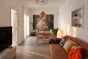 Un salon moderne avec un téléviseur, un coin repas comprenant une table et des chaises, et un canapé agrémenté de coussins colorés.
