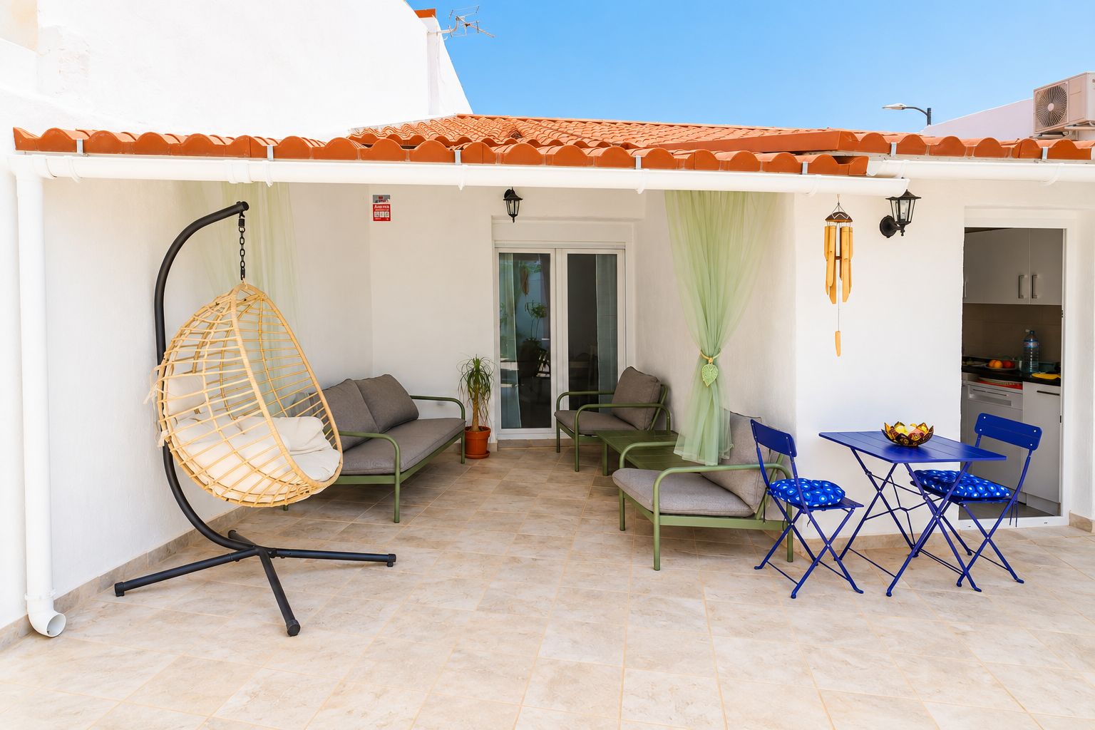 A patio with a hanging chair, two sofas, a table with chairs, and a potted plant.